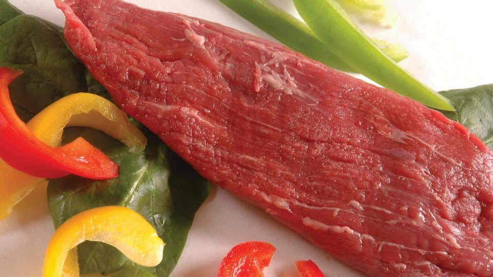 slab of beef with sliced peppers around it