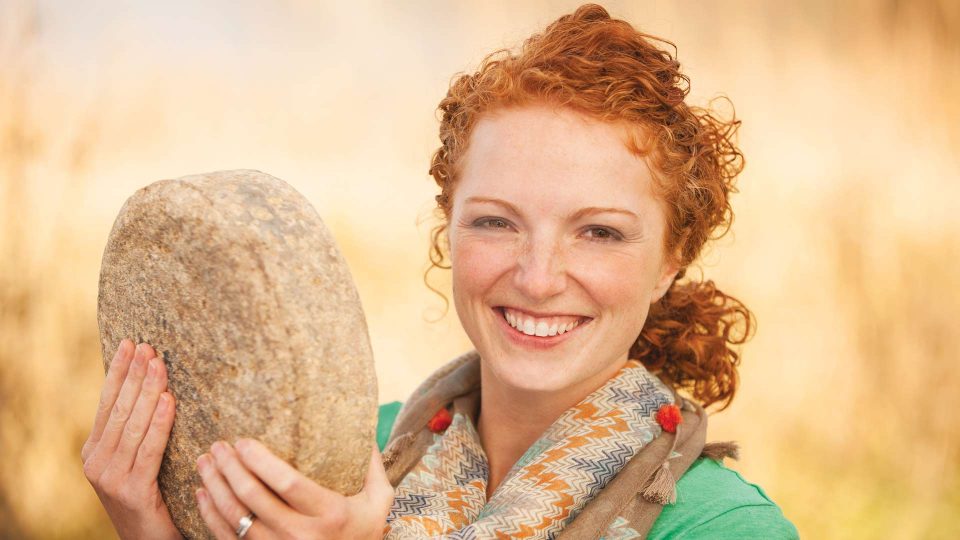 girl with red hair holding up a large cheese round