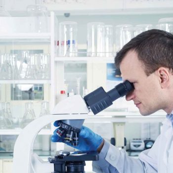 scientist in white lab coat looking into a microscope